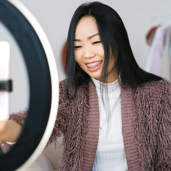 Smiling woman using smartphone and ring light for live streaming indoors.